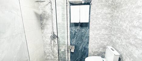 A modern bathroom with a glass-enclosed shower, a white toilet, and marble walls.