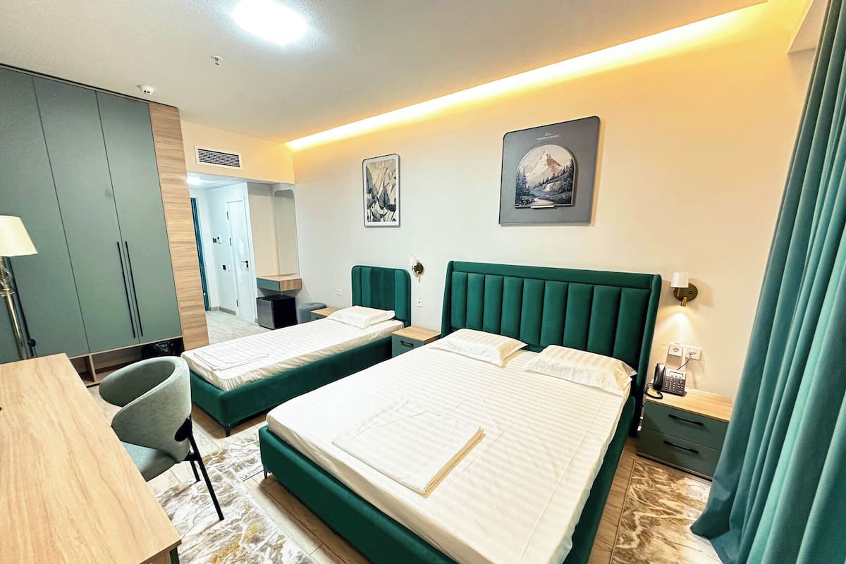 Quarto de hotel com duas camas, uma escrivaninha, uma cadeira, um guarda-roupa e um banheiro.