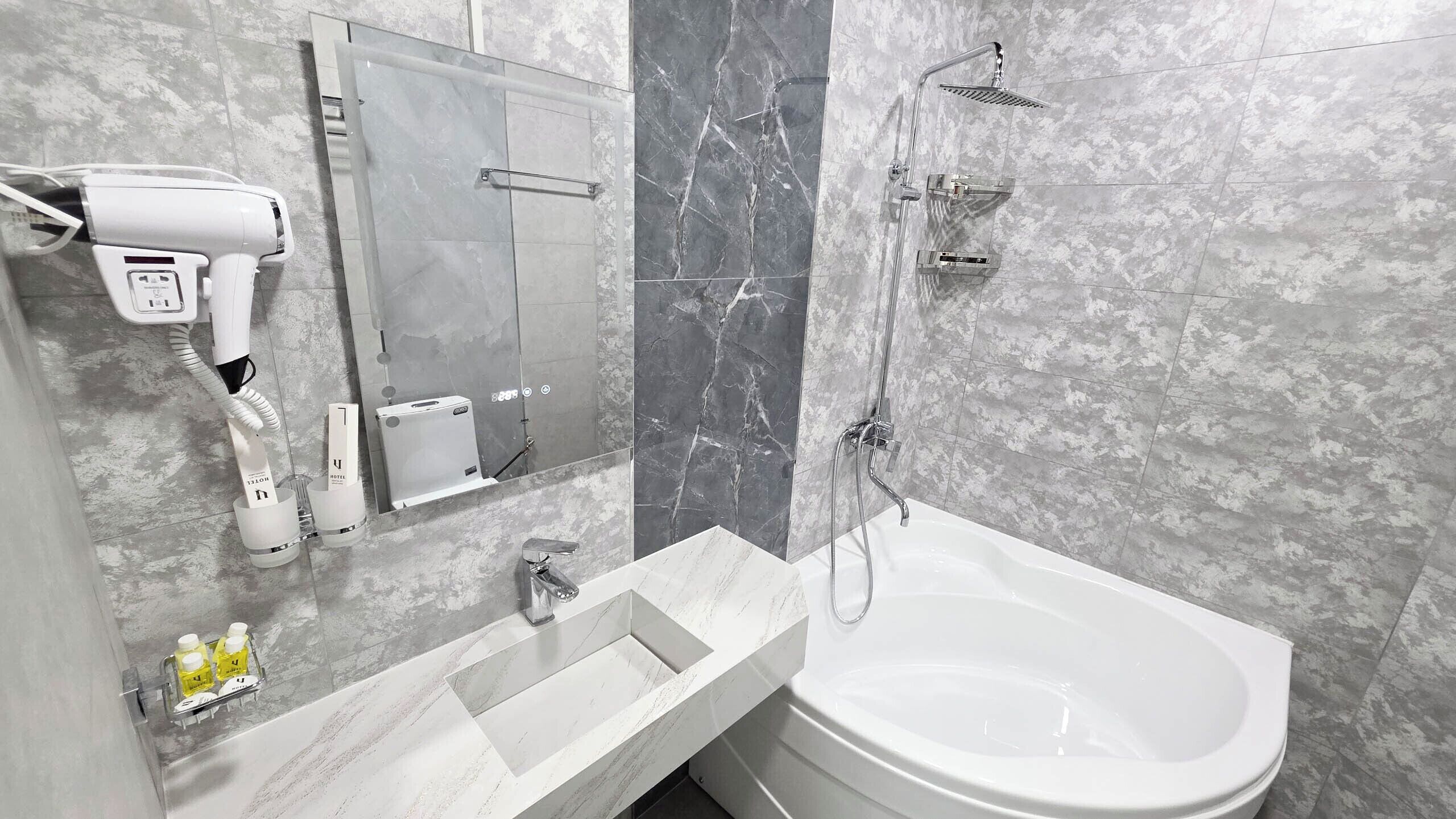 A bathroom with a bathtub, a hairdryer, and a mirror.
