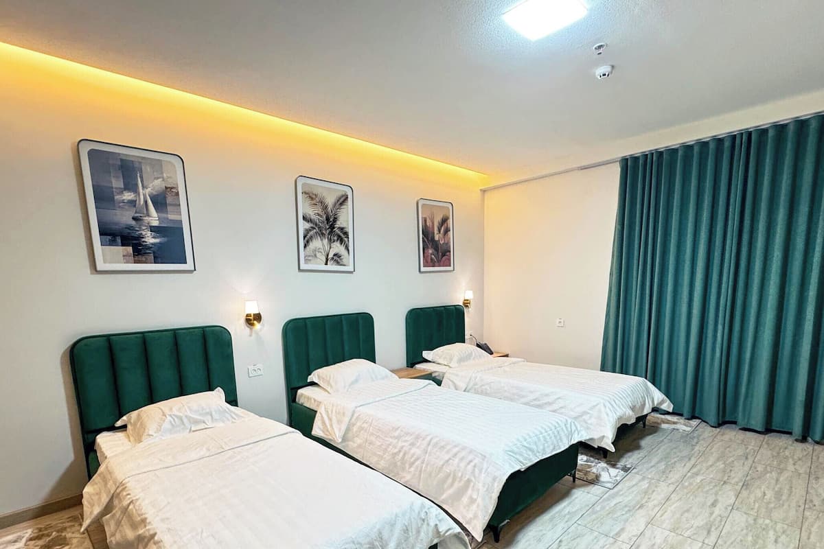 Quarto de hotel com duas camas, uma janela grande com cortinas e obras de arte fixadas na parede.