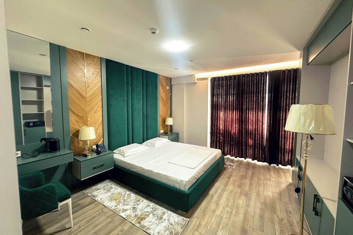 Quarto moderno com cama, mesas de cabeceira, escrivaninha e uma cadeira.