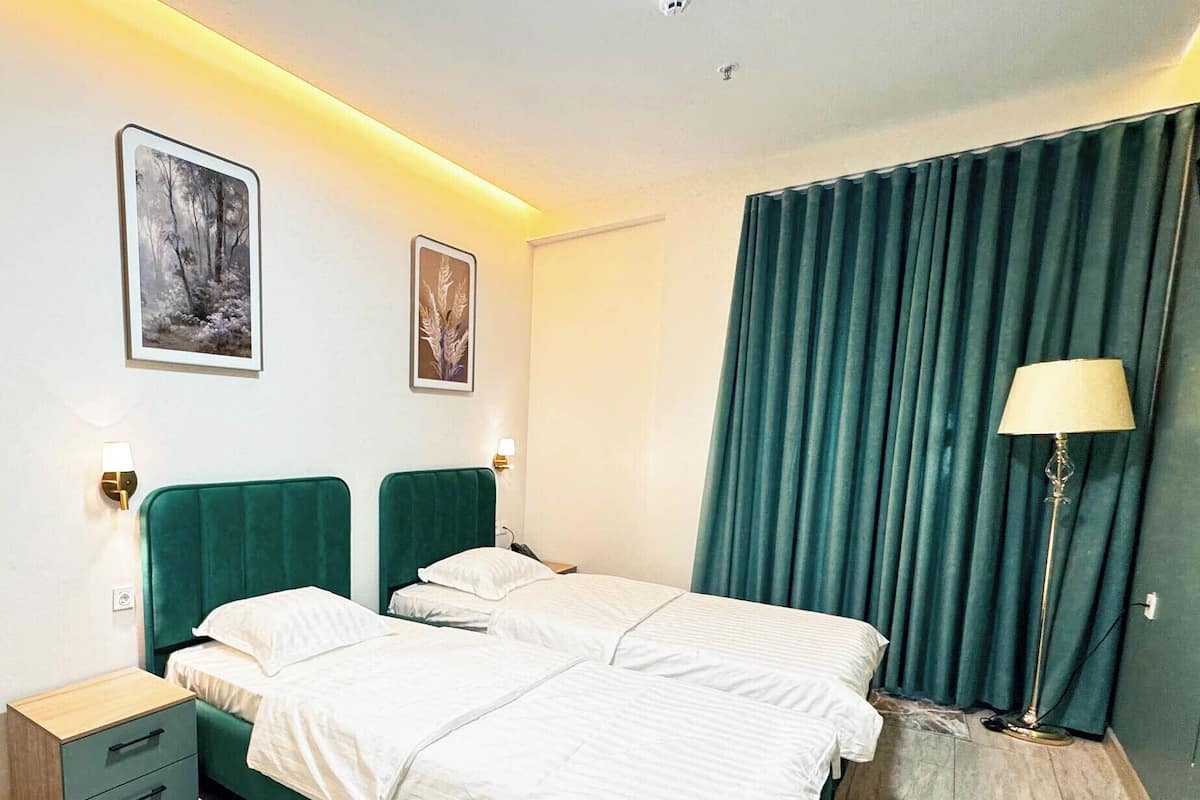 Quarto moderno com cama verde, duas mesinhas de cabeceira, um abajur e duas imagens emolduradas na parede.