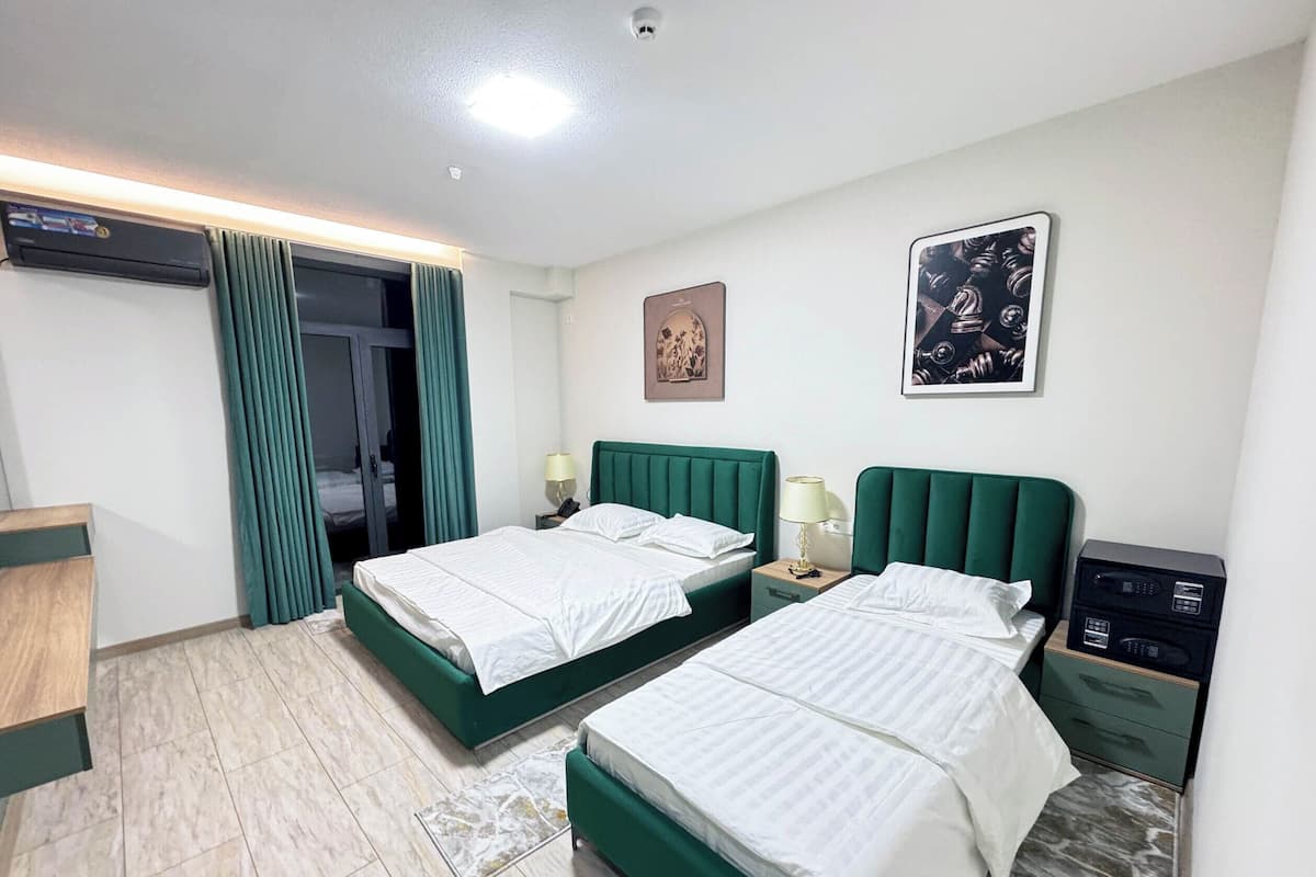 Quarto de hotel com duas camas, uma escrivaninha, uma cadeira, um guarda-roupa, um espelho e uma luminária no teto.