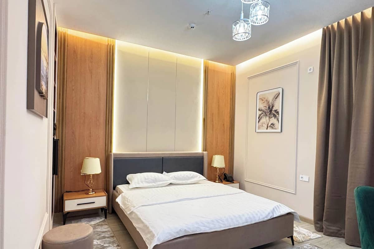 Quarto de hotel moderno com uma cama grande, luminárias de cabeceira, mesa de cabeceira, um banquinho redondo e um lustre.