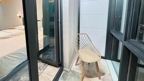 Habitación de hotel con cama, una silla, puerta corredera y vista al exterior.