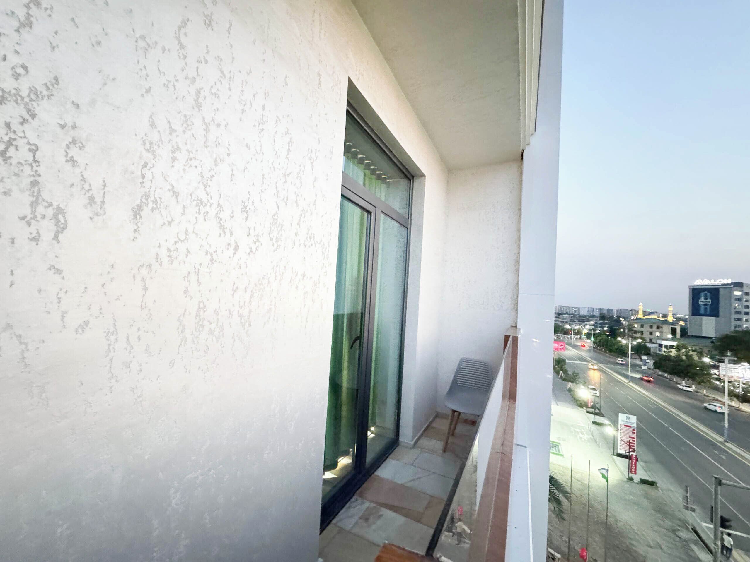 Un balcon donnant sur une rue de la ville, une chaise et un bâtiment sur lequel on peut lire le mot « AVALON ».