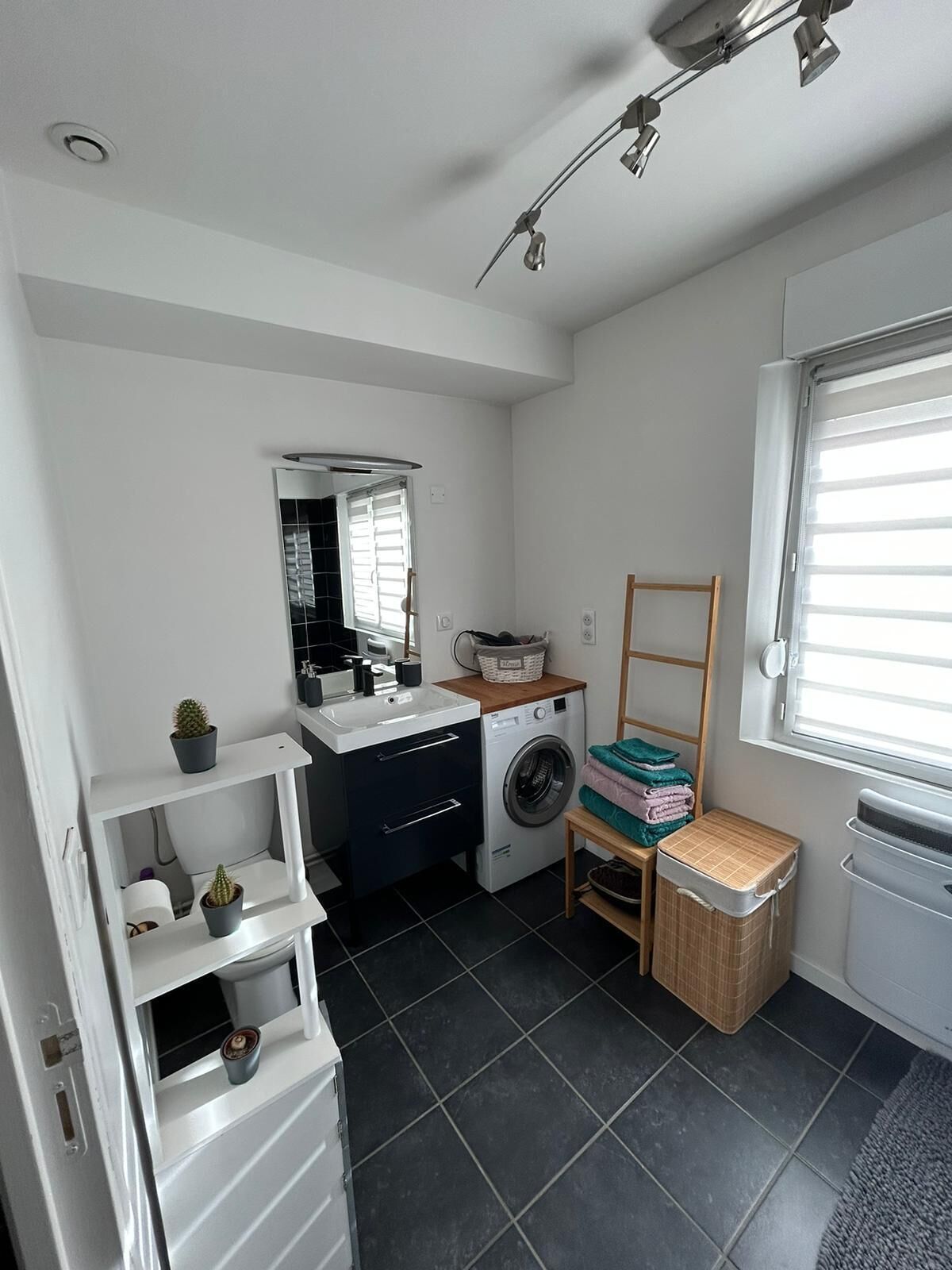 Een kleine wasruimte met een wasmachine, een droogrek en planken met planten.