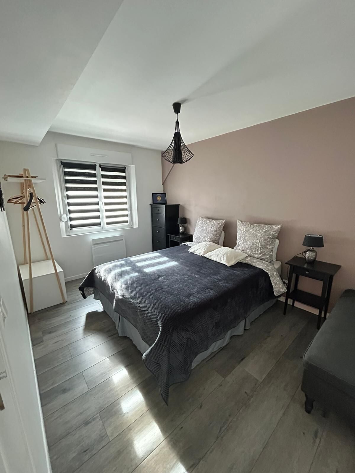 Ein Schlafzimmer mit Bett, Nachttisch, Lampe, Fenster mit Jalousien, einer Leiter und einem Deckenventilator.