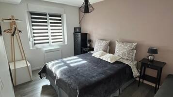 Ein Schlafzimmer mit Bett, Nachttisch, Lampe, Fenster mit Jalousien, einer Leiter und einem Deckenventilator.