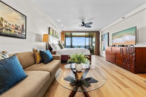 A modern hotel room with a bed, sofa, TV, and a balcony with a view. - Junior Suite Oceanfront #903 (Lahaina)