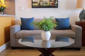 A living room with a sofa, a glass coffee table, and a potted plant. - Junior Suite Oceanfront #903 (Lahaina)