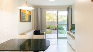 A modern living room with a dining table, a sofa, a TV, and a sliding glass door leading to a balcony. - Aquarius Residence (Ipojuca)