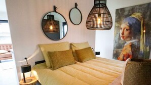A bedroom with a bed, bedside lamps, a round mirror, and a painting on the wall. - Wellness Lodge 2 (Olburgen)