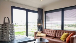 A modern living room with a leather sofa, a round coffee table, and a large window with blinds. - Wellness Lodge 2 (Olburgen)