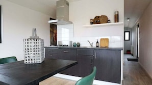 A modern kitchen with dark cabinets, a central island, and a dining area with green chairs. - Wellness Lodge 2 (Olburgen)