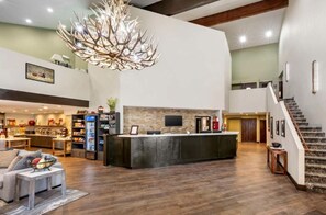 Eine geräumige Lobby mit einer zentralen Insellounge, einer Treppe und einem Küchenbereich im Hintergrund.