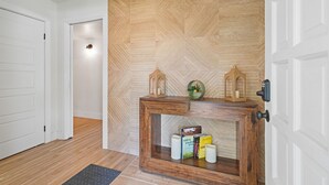 Een gang met een houten visgraatwand, een console tafel met boeken en kaarsen, en een deur met een zwarte handgreep.
