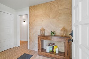 Ein Flur mit einer Wand aus Holzvertäfelung im Fischgrätmuster, einem Konsolentisch mit Büchern und Kerzen sowie einer Tür mit schwarzem Griff.