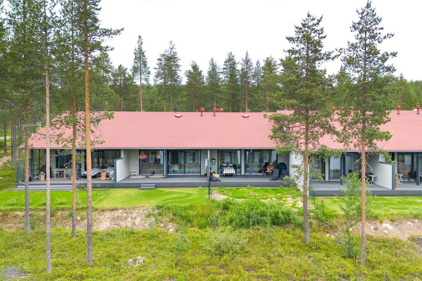 A modern building with a red roof, large glass windows, and a covered outdoor area with seating.
