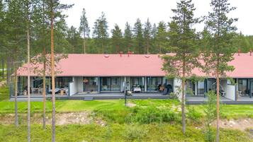 A modern building with a red roof, large glass windows, and a covered outdoor area with seating.