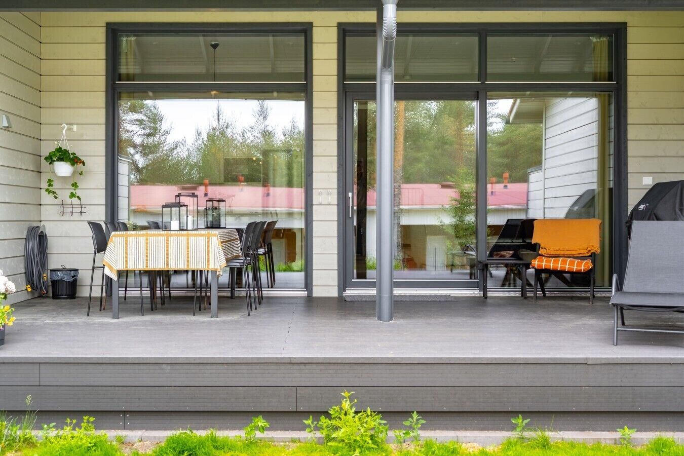 Eine überdachte Terrasse mit Esstisch, Stühlen, Grill und einer hängenden Pflanze.
