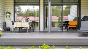 En overdækket terrasse med spisebord, stole, grill og en hængende plante.