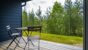 Una terraza de madera con una mesa y dos sillas, con vistas a un bosque.