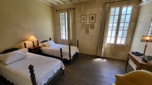 A room with two wooden beds, a chair, a table, and a window with curtains.