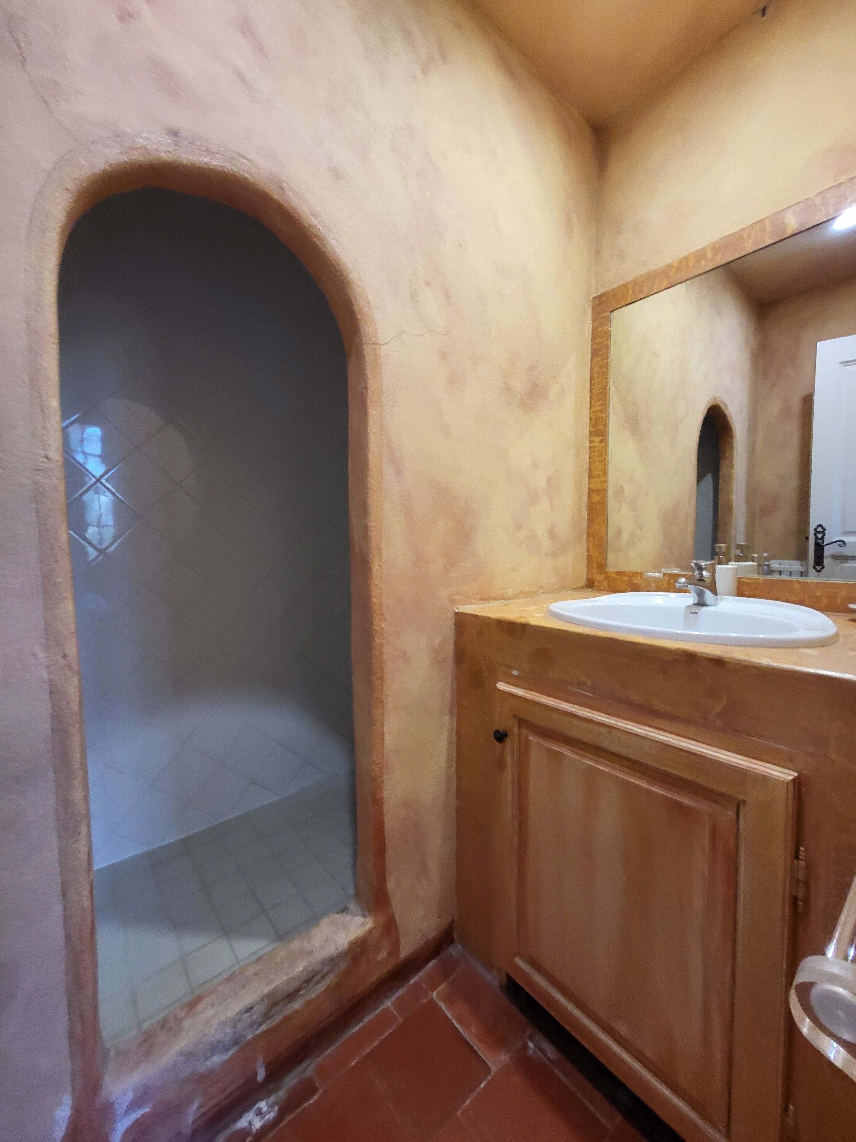 Un baño con lavabo, espejo y puerta en arco.