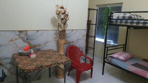 A room with a bunk bed, a table with a patterned tablecloth, a red plastic chair, a decorative vase with dried flowers, and a mirror on the wall. - Dazhong Backpacker's Hostel (Medan)