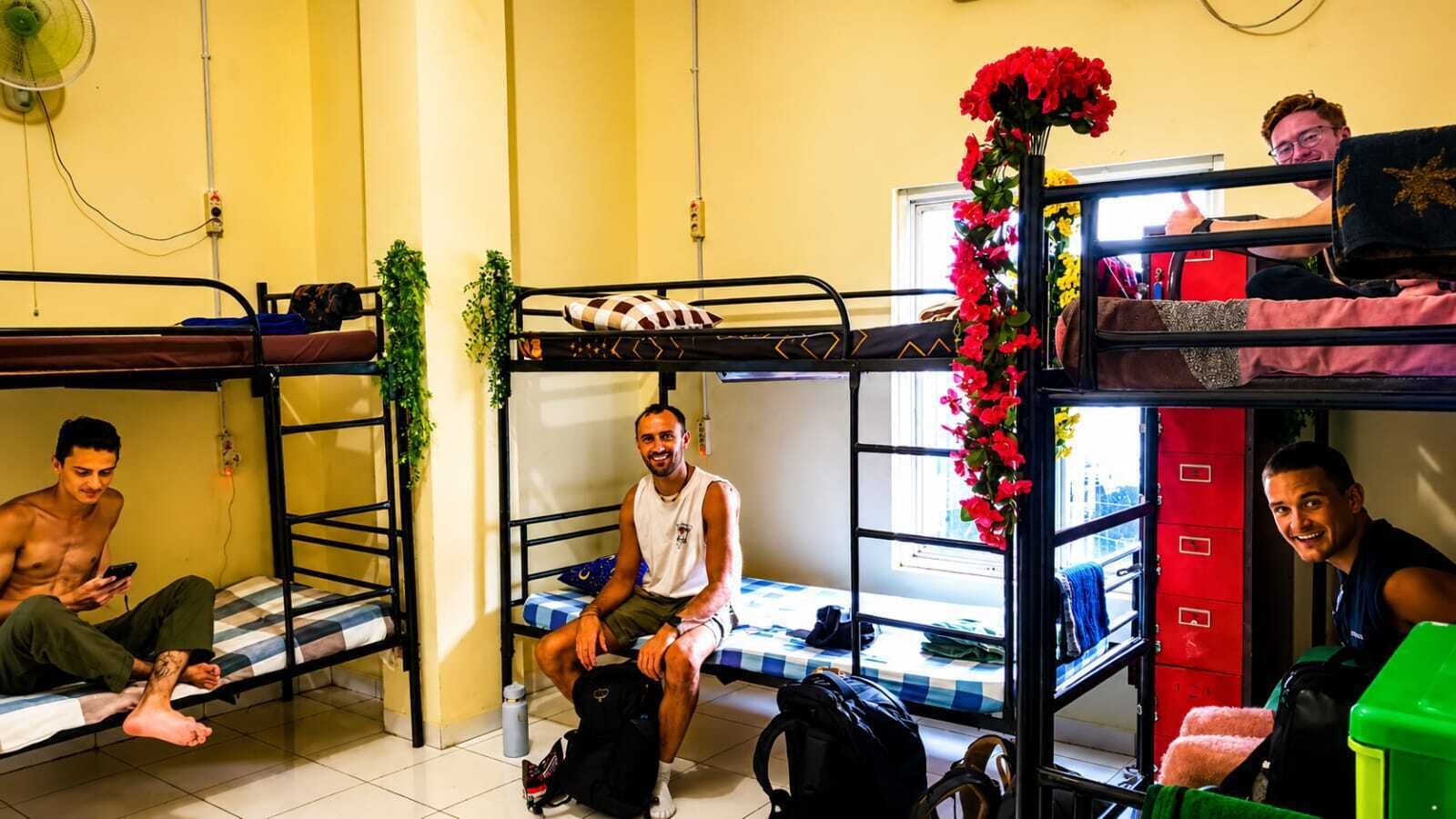 A dormitory room with bunk beds, a fan, a window, and a red flower decoration.