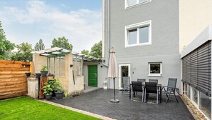 A residential building with a patio area, a green door, and a small garden.