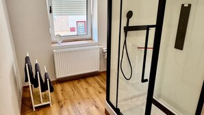 A modern bathroom with a glass shower enclosure, a wooden floor, a radiator, and a window with blinds. - Room 'Ferienzimmer Nala und Loft' for Families and Holiday Guests (Görlitz)