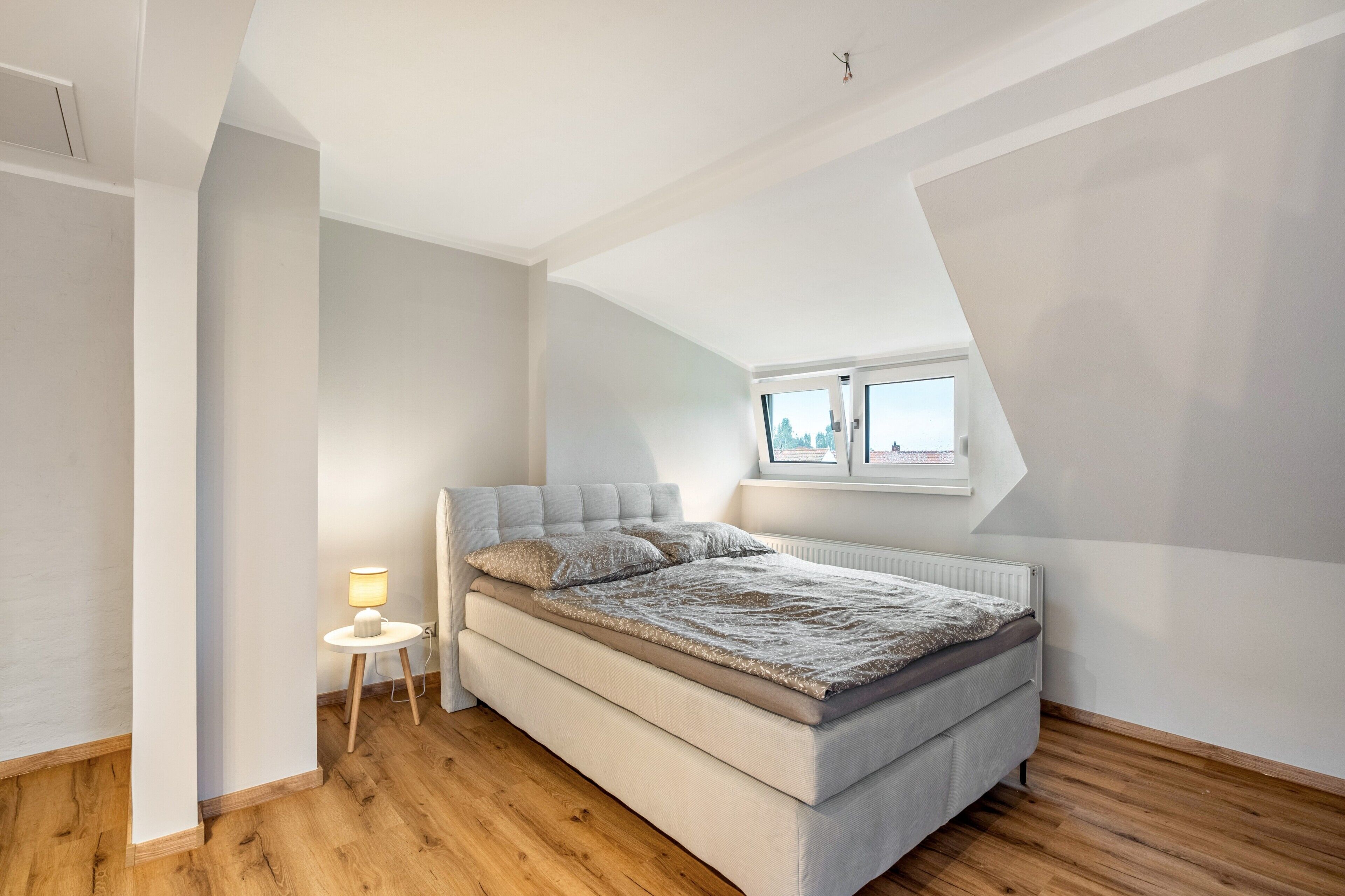 Une chambre à coucher avec un lit, une table de chevet avec une lampe et une fenêtre.