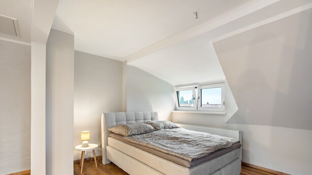 A bedroom with a bed, a bedside table with a lamp, and a window. - Room 'Ferienzimmer Nala und Loft' for Families and Holiday Guests (Görlitz)