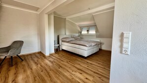 A bedroom with a bed, a chair, a small table, and a window with blinds.