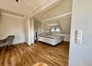 A bedroom with a bed, a chair, a small table, and a window with blinds.