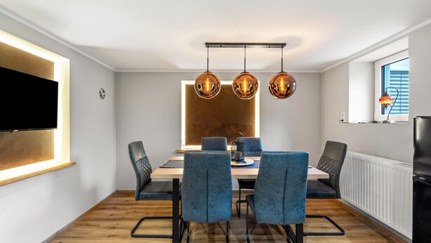 A modern dining area with a wooden table, blue upholstered chairs, and pendant lights.
