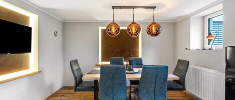 A modern dining area with a wooden table, blue upholstered chairs, and pendant lights.