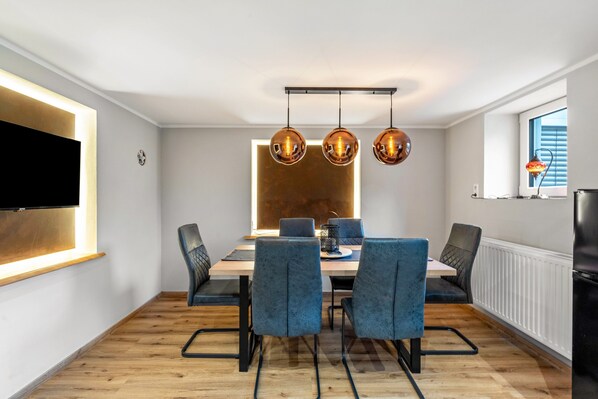 A modern dining area with a wooden table, blue upholstered chairs, and pendant lights.