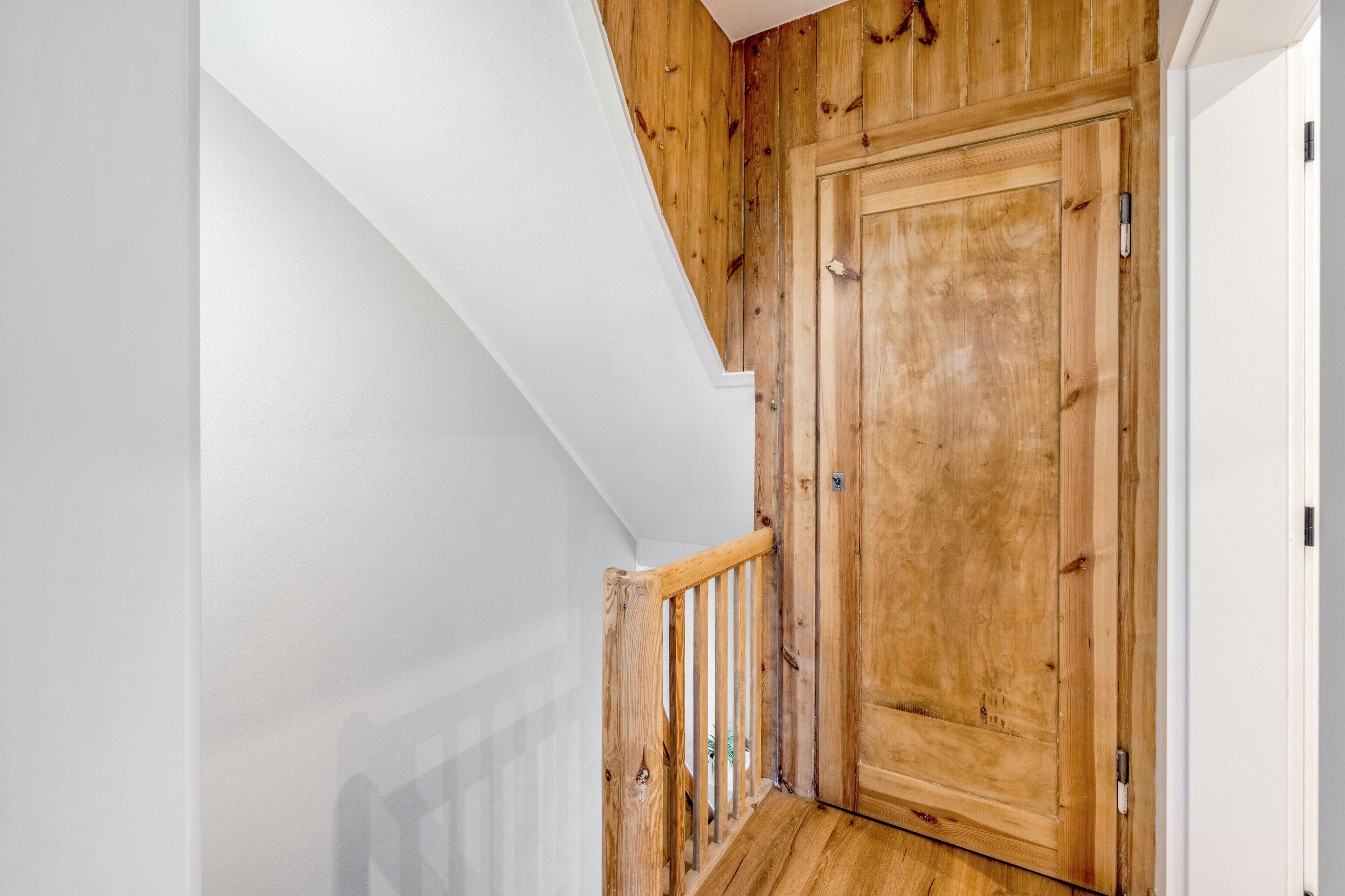 Una escalera de madera, con una pared blanca a un lado y una puerta de madera al otro.