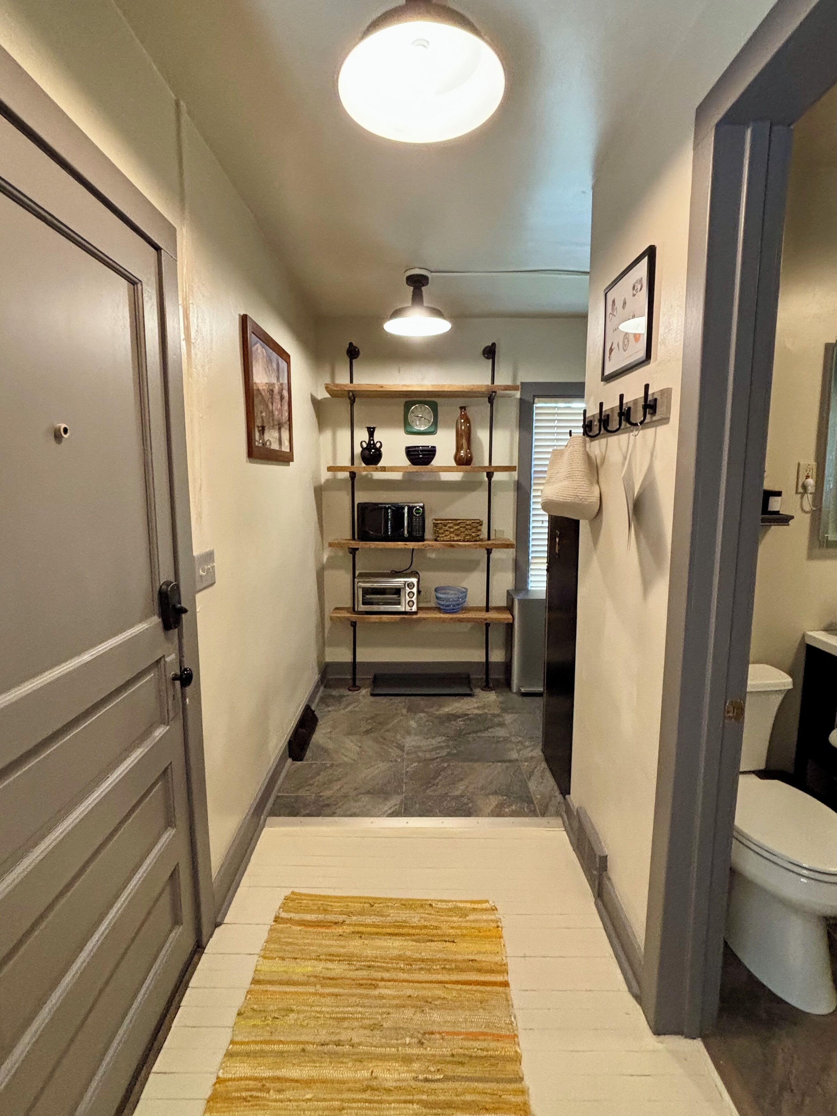 Un couloir étroit avec un banc en bois, un four à micro-ondes et une petite étagère ornée d’objets décoratifs.