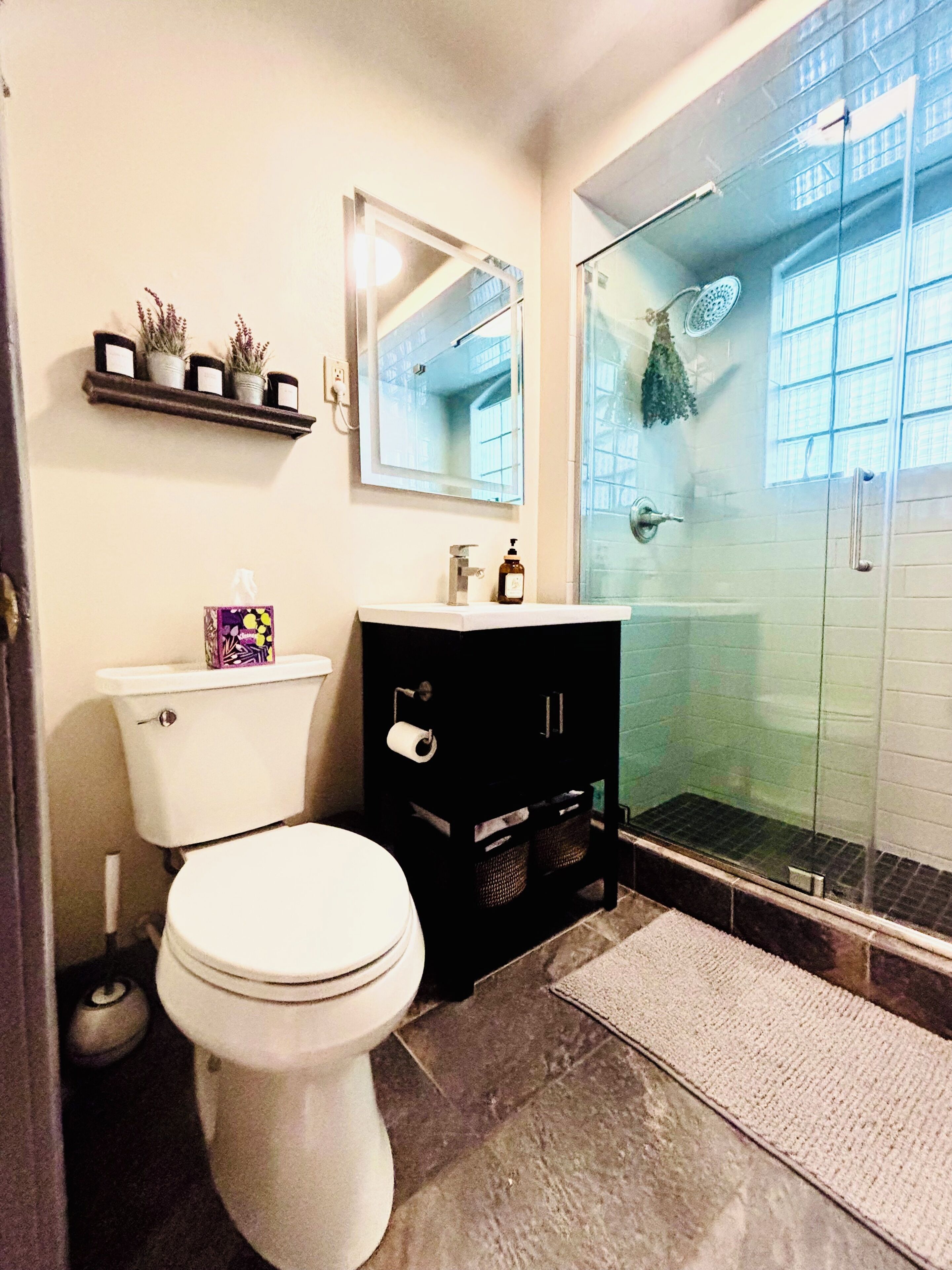 Une salle de bain comprenant des toilettes, un meuble-lavabo noir, un miroir et une douche à parois de verre.