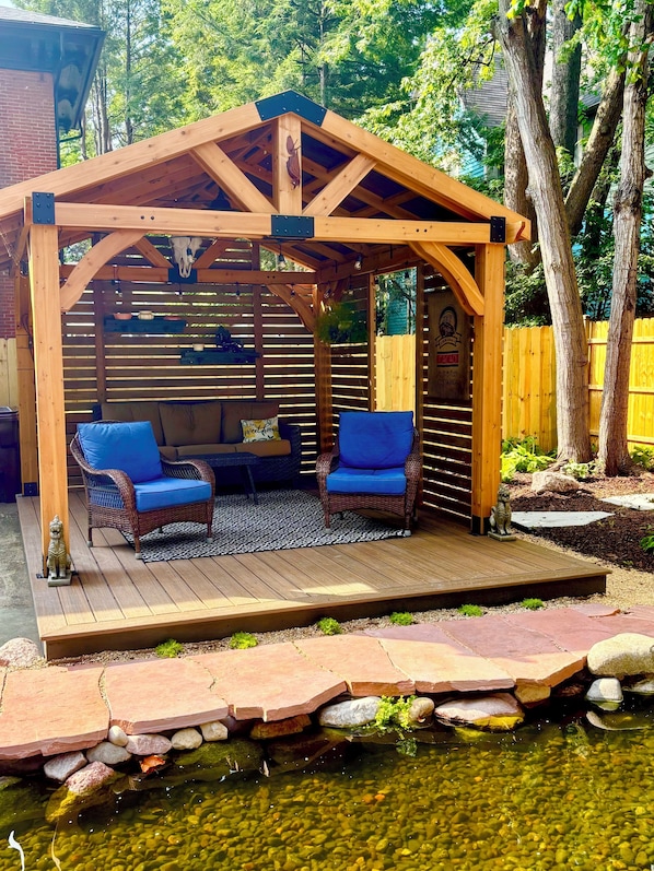 A wooden pergola with a seating area, a pond, and a wooden deck.