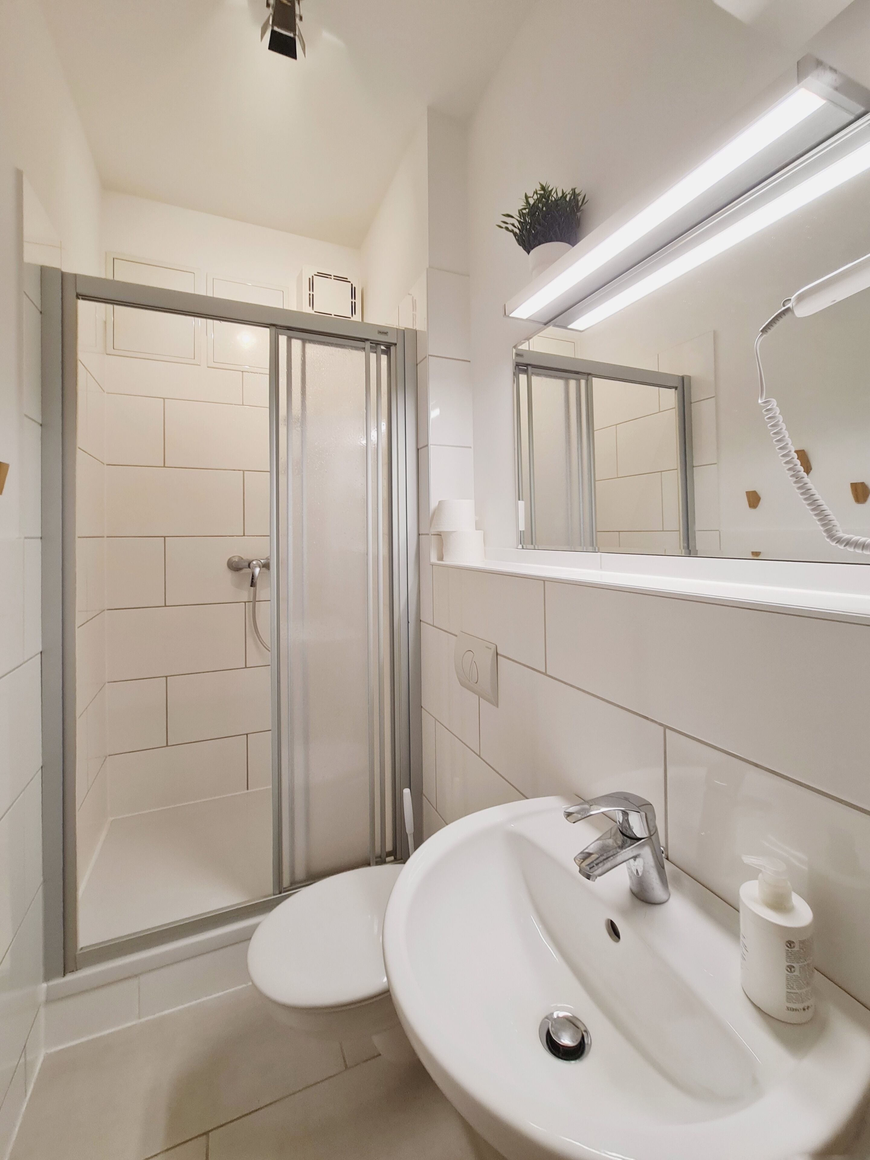 Un baño moderno con cabina de ducha de vidrio, un lavamanos blanco y un espejo sobre él.