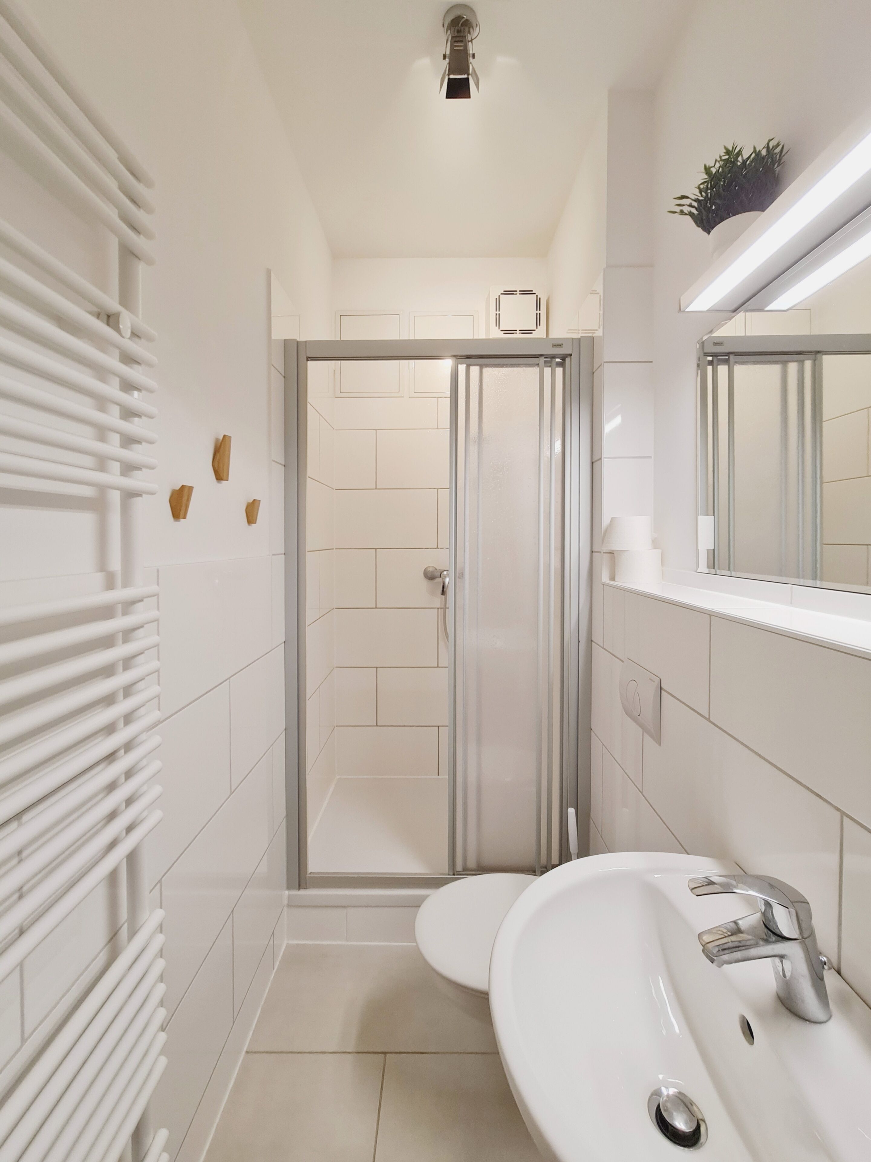 Une salle de bain moderne avec une douche à parois de verre, un lavabo blanc doté d’un robinet chromé et un miroir au-dessus du lavabo.