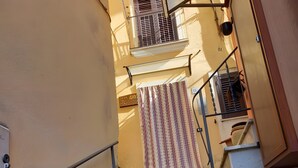 Eine schmale Treppe mit Metallgeländer, einem Streifenmuster-Vorhang und einem kleinen Balkon mit einem Fenster.