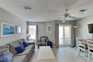Ein Wohnzimmer mit Sofa, Sessel, Esstisch, Deckenventilator und Kunstwerken an den Wänden.