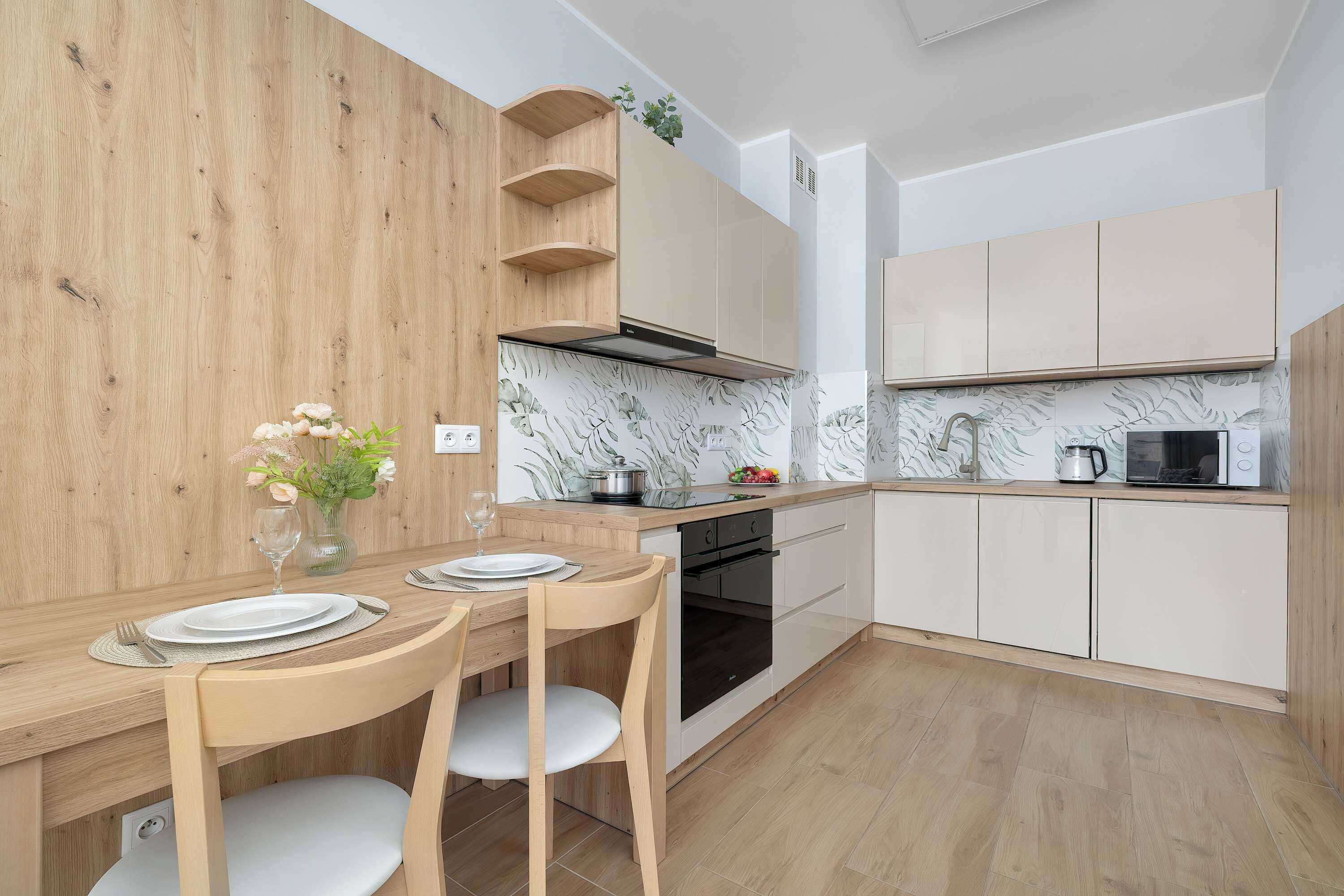 Une cuisine moderne avec des meubles en bois, un four encastré et un coin repas avec une table mise pour deux personnes.