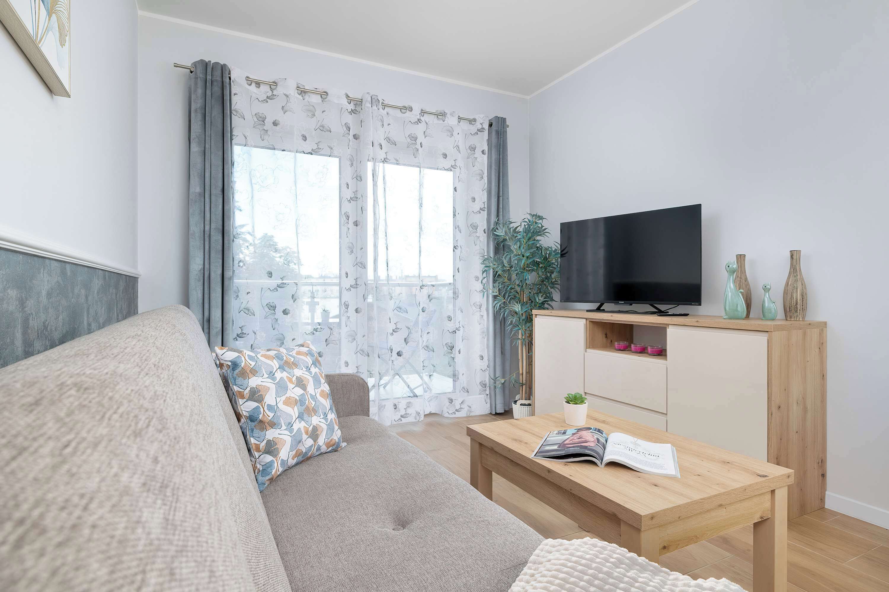 Ein Wohnzimmer mit einer Couch, einem Couchtisch, einem Fernseher auf einem Holzboden und einem Fenster mit Vorhängen.